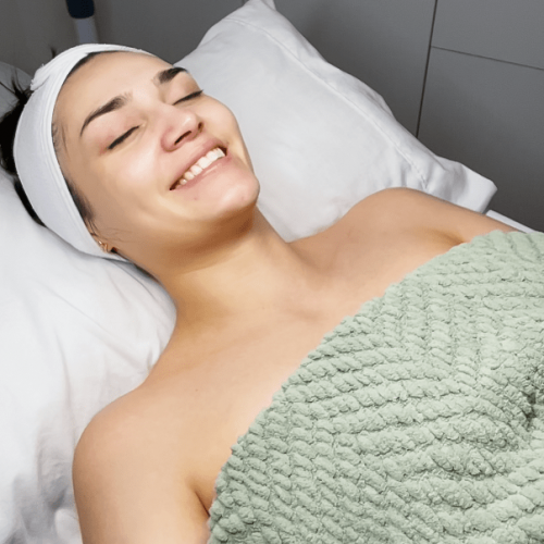 A smiling woman laying on a pillow wrapped in a towel